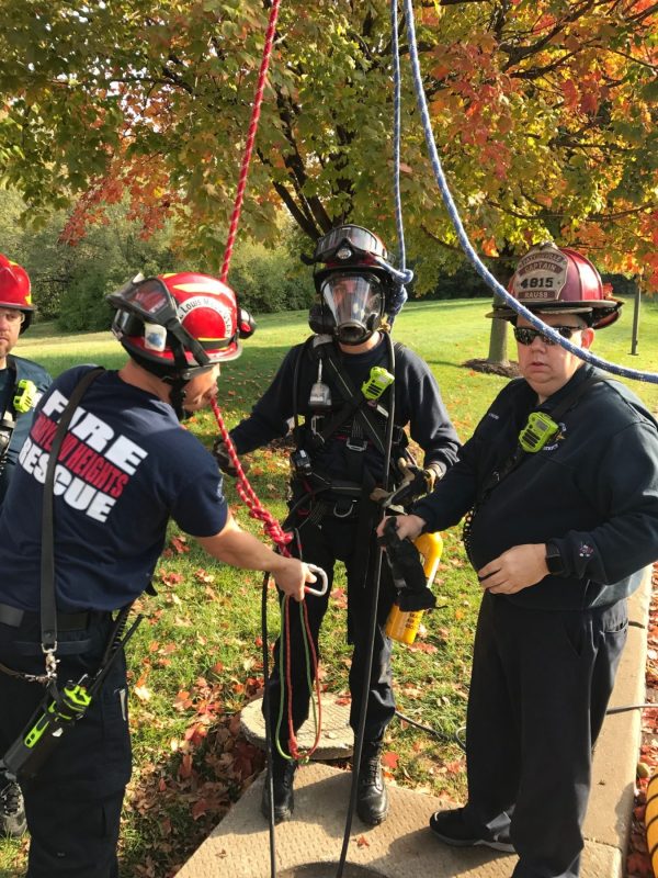 Firefighters over storm sewer with ropes